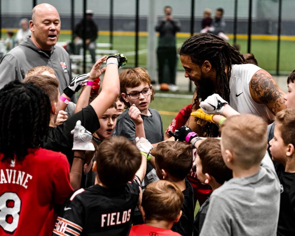 Two coaches leading a huddle of youth football players on an indoor turf field