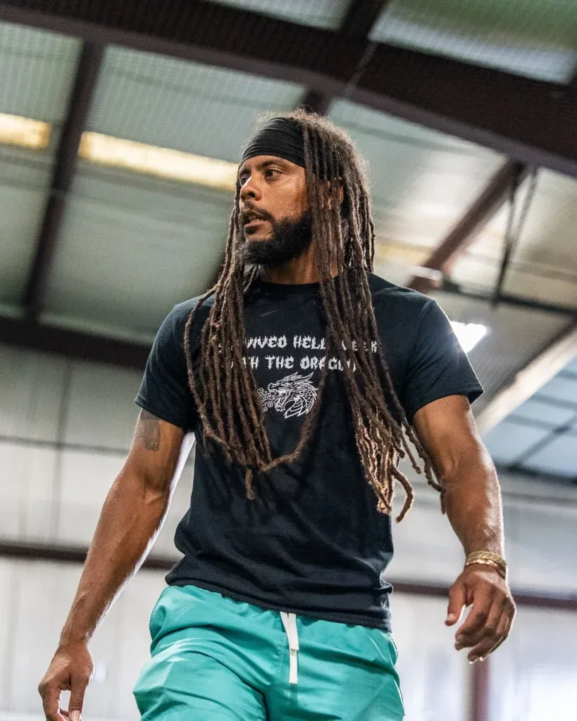 Coach Davion in a black shirt and teal shorts looking across the indoor training facility