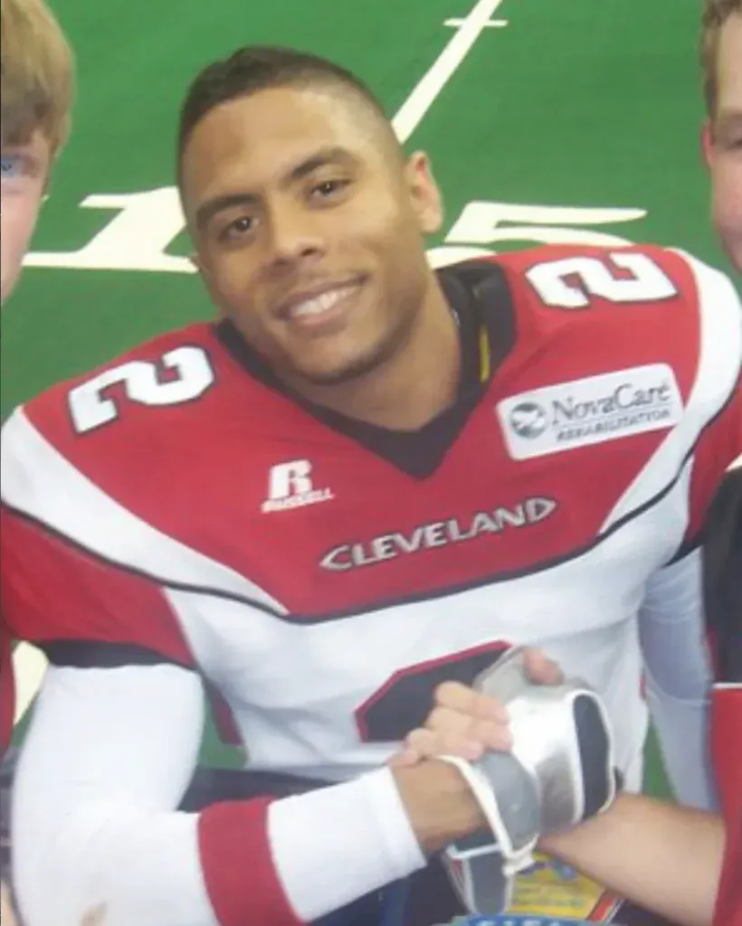 Smiling football player in a red and white Cleveland number 2 jersey shaking hands with fans on an indoor field